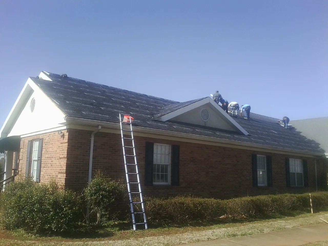 Crew tearing shingles off a brick ranch roof with a ladder set — Emergency Roof Repair work by our crew in Como