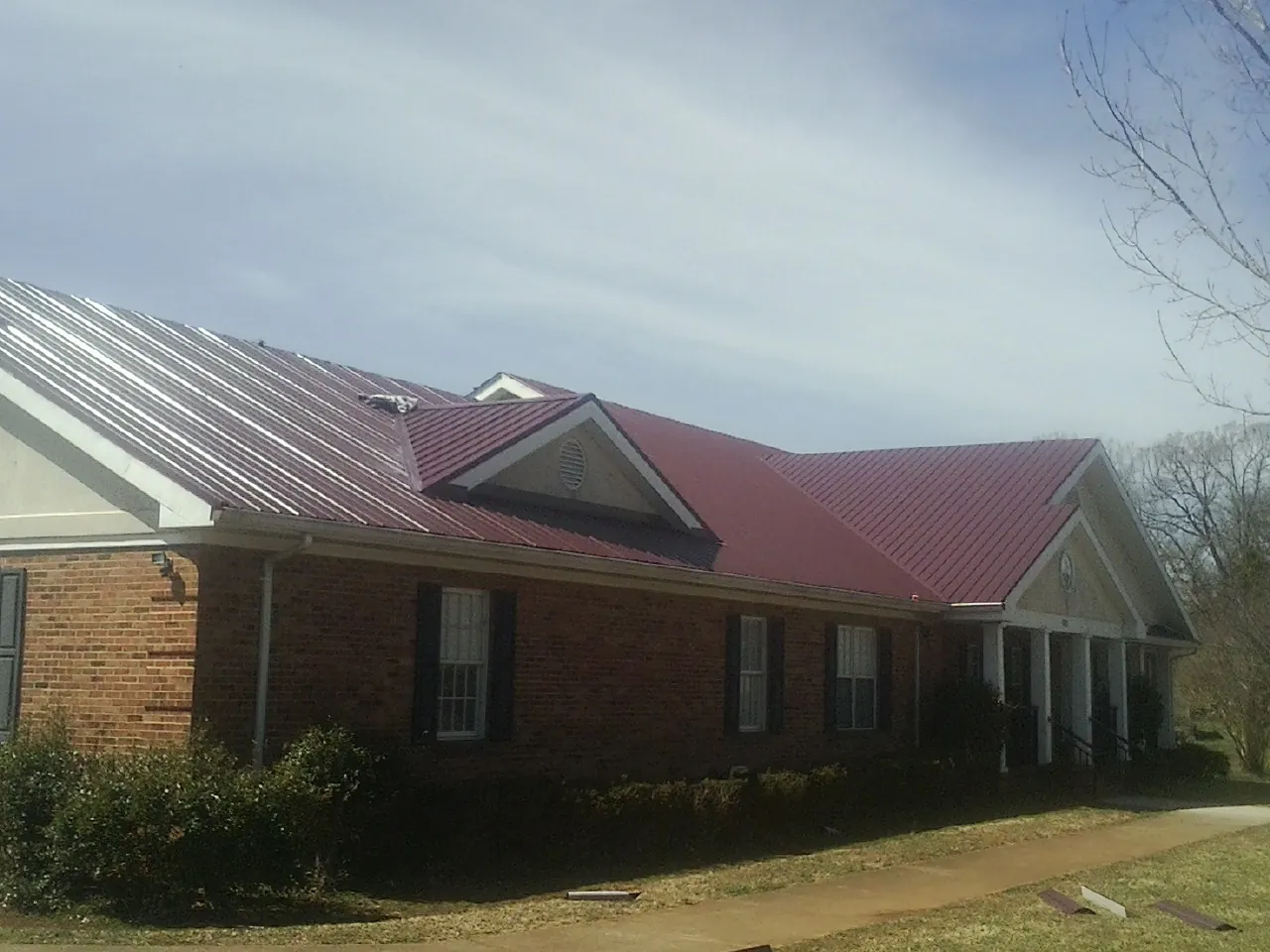 Red metal roof with gabled entries on a long brick building, from a Hail Damage Roof Repair job in Como