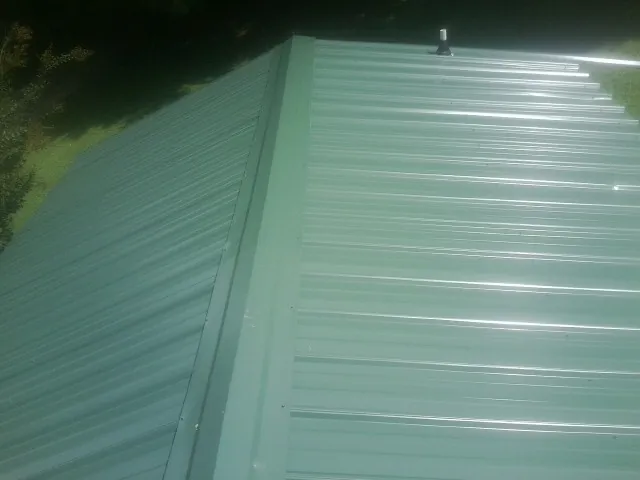 New green metal panels meeting at the ridge of a roof — Flat Roof Repair work by our crew in Como