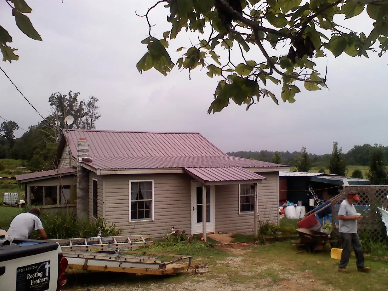 Crew finishing a mauve metal roof on a small farmhouse in Como